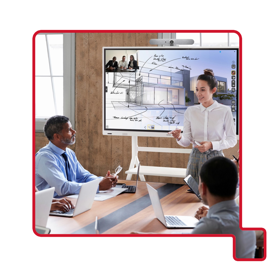 A woman presents architectural plans on a digital whiteboard to colleagues in a modern conference room with laptops.